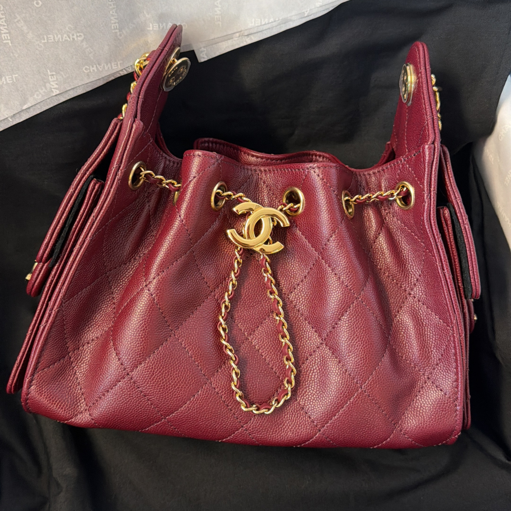 A red quilted leather shoulder bag with gold-tone hardware, featuring a prominent interlocking CC logo on a chain strap, resting on a black fabric surface.