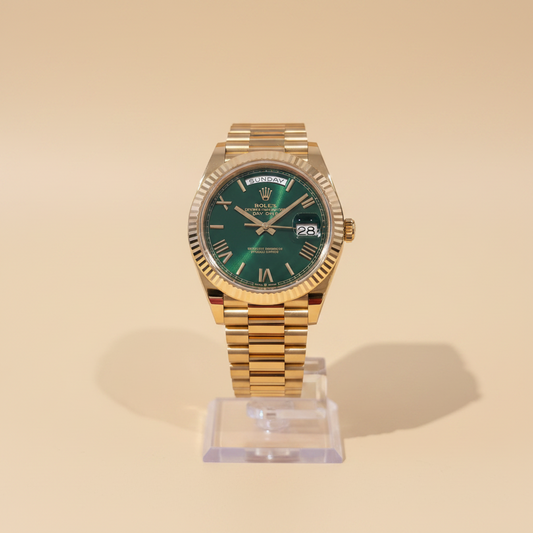 A Rolex watch with a gold-tone jubilee bracelet and green dial is held in a hand, positioned in front of an open cream-colored Rolex presentation box.